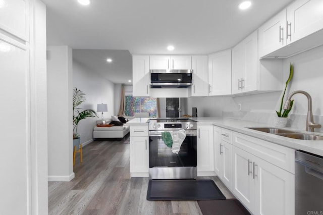 kitchen featuring kitchen peninsula, appliances with stainless steel finishes, sink, white cabinets, and light hardwood / wood-style floors