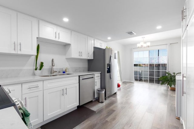 kitchen featuring appliances with stainless steel finishes, sink, an inviting chandelier, white cabinets, and light hardwood / wood-style floors