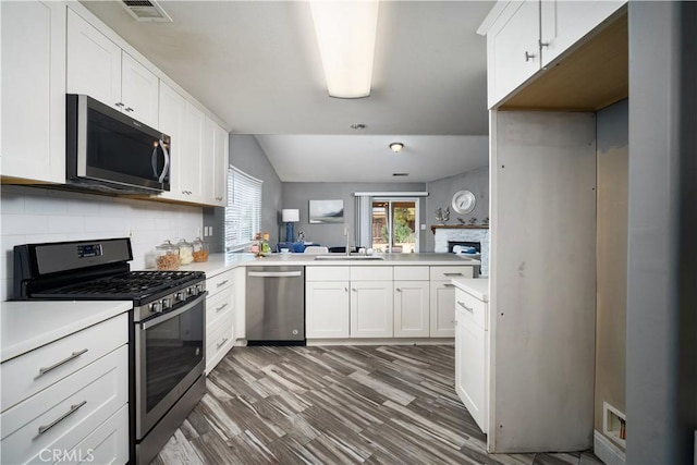 kitchen with white cabinets, kitchen peninsula, appliances with stainless steel finishes, and tasteful backsplash