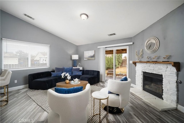 living room featuring wood-type flooring, vaulted ceiling, and a stone fireplace