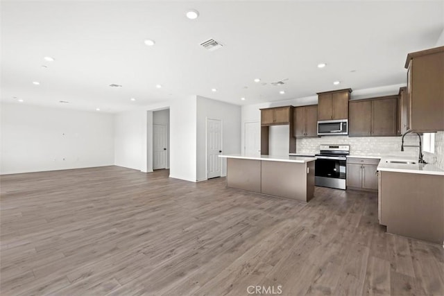 kitchen with tasteful backsplash, a kitchen island, sink, hardwood / wood-style flooring, and appliances with stainless steel finishes