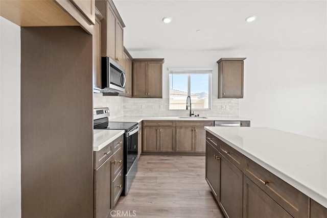 kitchen featuring stainless steel appliances, decorative backsplash, light hardwood / wood-style flooring, and sink