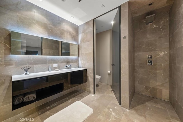 bathroom with vanity, toilet, tiled shower, and tile walls