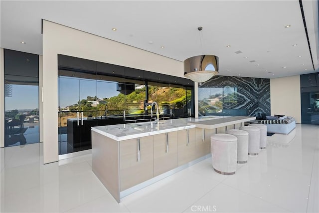 kitchen featuring a breakfast bar area, a center island with sink, light tile patterned floors, and hanging light fixtures