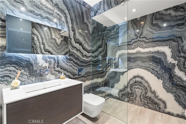 bathroom featuring a tile shower, vanity, tile walls, and toilet