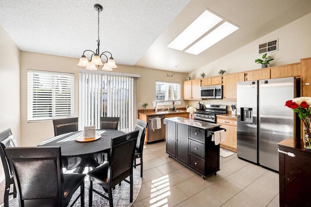 kitchen featuring light brown cabinets, hanging light fixtures, vaulted ceiling with skylight, a kitchen island, and stainless steel appliances