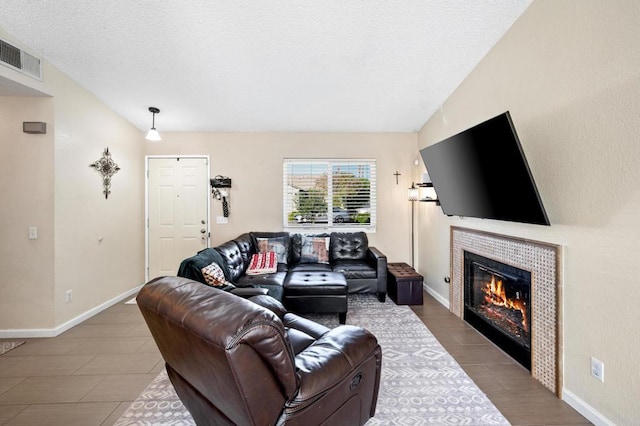 living room with tile patterned floors, vaulted ceiling, a textured ceiling, and a tiled fireplace