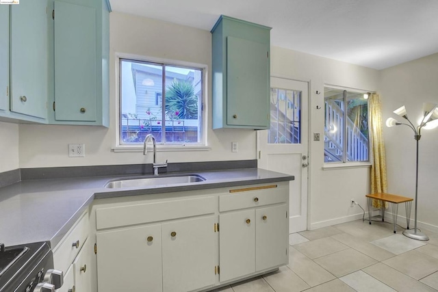 kitchen with light tile patterned flooring, range, white cabinets, and sink