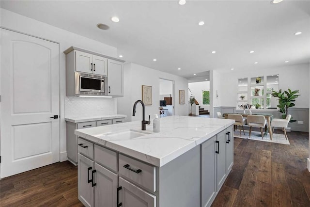 kitchen featuring light stone counters, stainless steel microwave, dark wood-type flooring, and sink