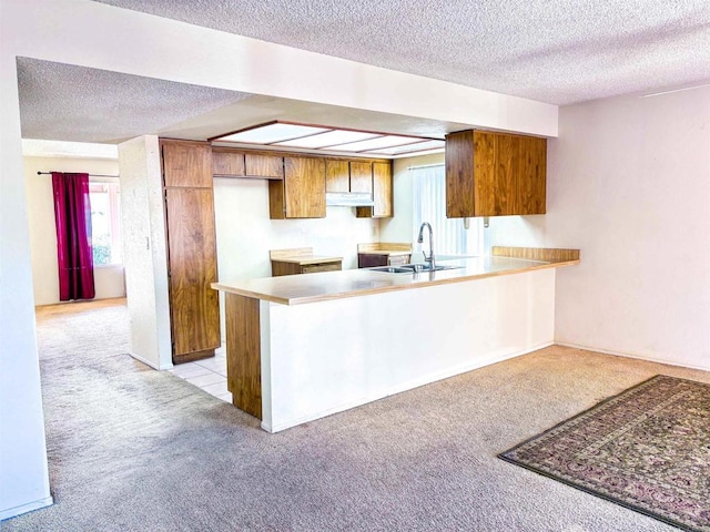 kitchen with a textured ceiling, sink, kitchen peninsula, and light carpet