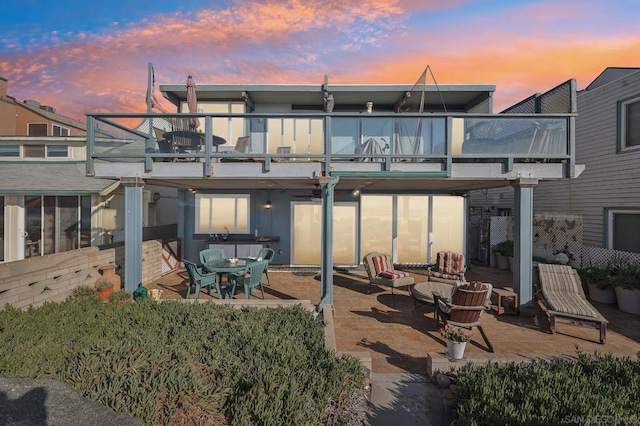 back house at dusk featuring a patio and a balcony