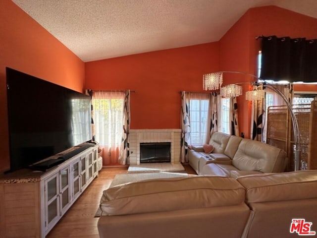 living room featuring a fireplace, plenty of natural light, light hardwood / wood-style floors, and vaulted ceiling