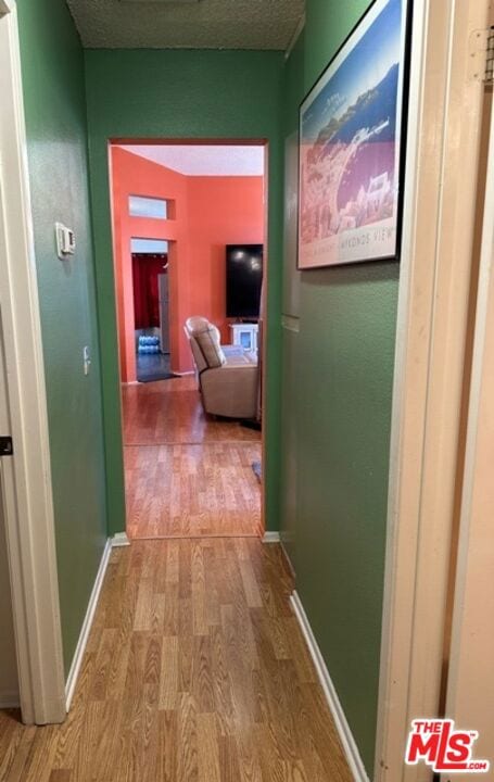 hallway with light wood-type flooring and a textured ceiling