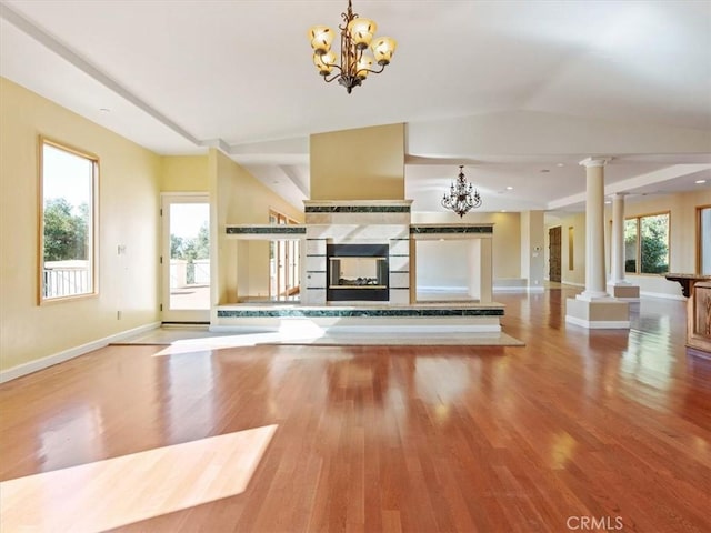 unfurnished living room featuring decorative columns, a tiled fireplace, hardwood / wood-style floors, and a notable chandelier