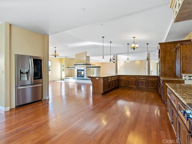 kitchen with hanging light fixtures, a notable chandelier, island range hood, stainless steel fridge with ice dispenser, and kitchen peninsula