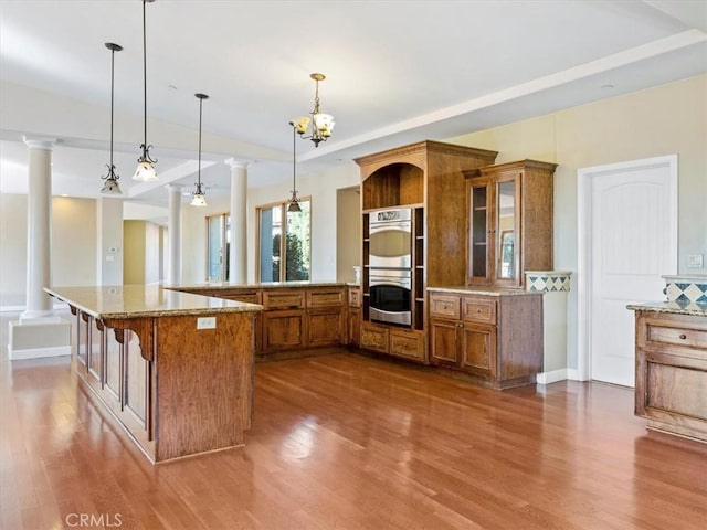 kitchen with ornate columns, a breakfast bar area, stainless steel double oven, and decorative light fixtures