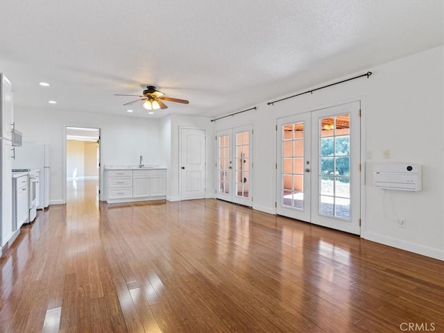 unfurnished living room featuring an AC wall unit, wood-type flooring, sink, ceiling fan, and french doors