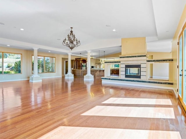 unfurnished living room featuring vaulted ceiling, decorative columns, and light wood-type flooring