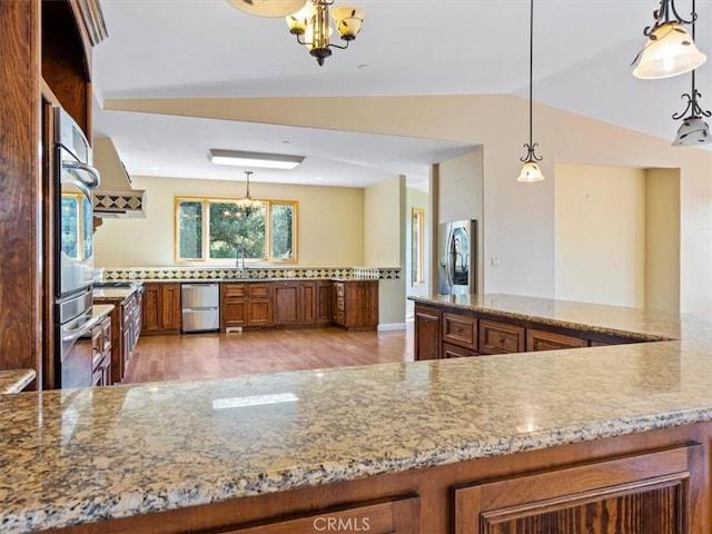 kitchen featuring pendant lighting, lofted ceiling, stainless steel appliances, and light hardwood / wood-style flooring