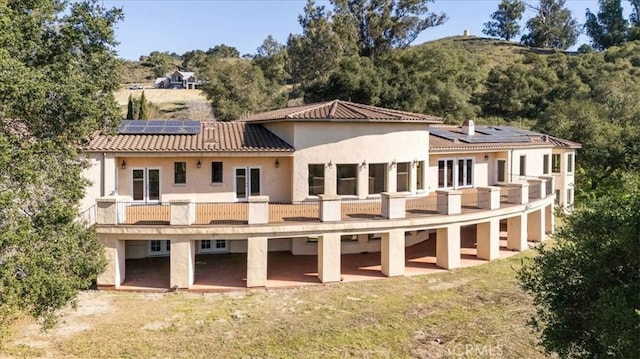 back of property featuring a balcony, a lawn, and solar panels