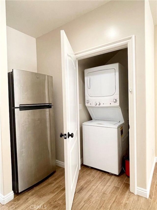 laundry area with light hardwood / wood-style floors and stacked washer and clothes dryer