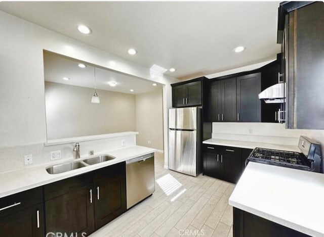 kitchen featuring appliances with stainless steel finishes, extractor fan, sink, light hardwood / wood-style floors, and hanging light fixtures