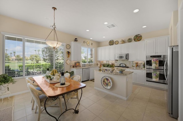 kitchen featuring white cabinets, appliances with stainless steel finishes, tasteful backsplash, decorative light fixtures, and a kitchen island