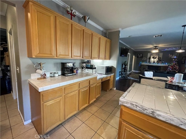 kitchen featuring ceiling fan, hanging light fixtures, tile countertops, crown molding, and light tile patterned floors