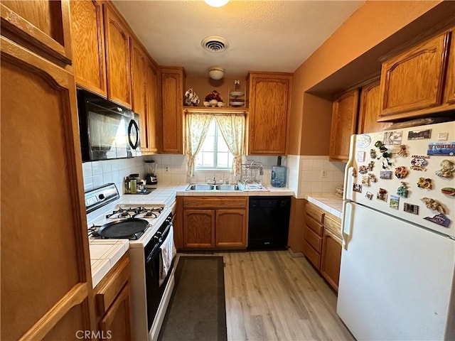 kitchen with decorative backsplash, light wood-type flooring, sink, black appliances, and tile countertops