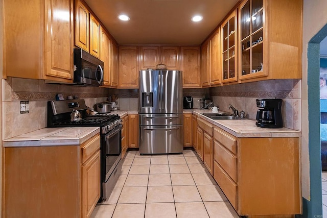 kitchen with tile countertops, light tile patterned floors, sink, and appliances with stainless steel finishes