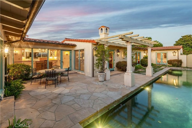 back house at dusk featuring a pergola and a patio