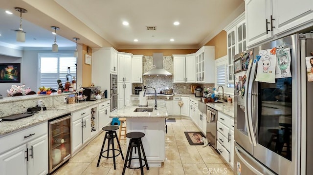 kitchen featuring appliances with stainless steel finishes, wall chimney exhaust hood, white cabinets, wine cooler, and an island with sink