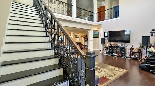 staircase featuring hardwood / wood-style floors, a towering ceiling, and ornate columns