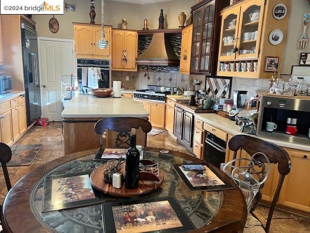 kitchen with black appliances, wall chimney exhaust hood, decorative backsplash, and light brown cabinetry