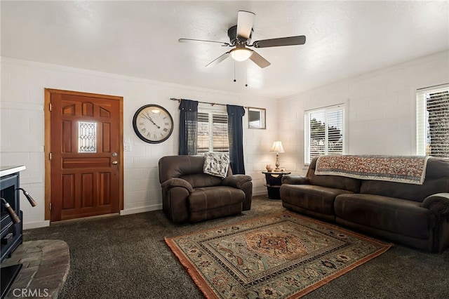 carpeted living area with a ceiling fan and concrete block wall