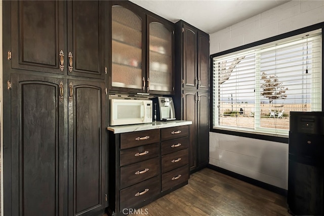 kitchen featuring dark wood-style flooring, white microwave, glass insert cabinets, light countertops, and dark brown cabinets
