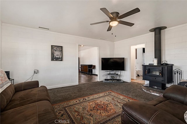 carpeted living room featuring ceiling fan, ornamental molding, and a wood stove