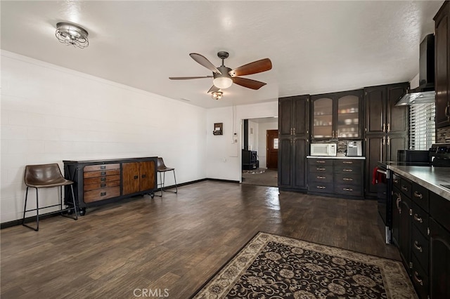 kitchen with wall chimney exhaust hood, black / electric stove, dark hardwood / wood-style floors, ceiling fan, and dark brown cabinetry