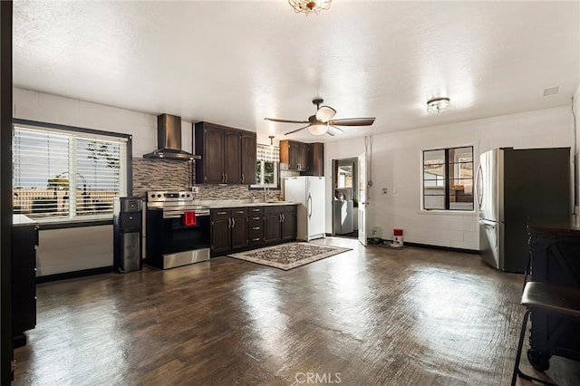 kitchen with stainless steel appliances, wall chimney exhaust hood, ceiling fan, tasteful backsplash, and dark brown cabinets