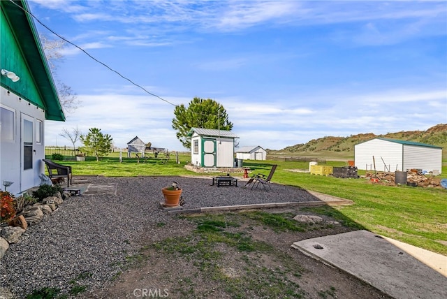view of yard with a storage shed, a patio area, a fire pit, and an outbuilding
