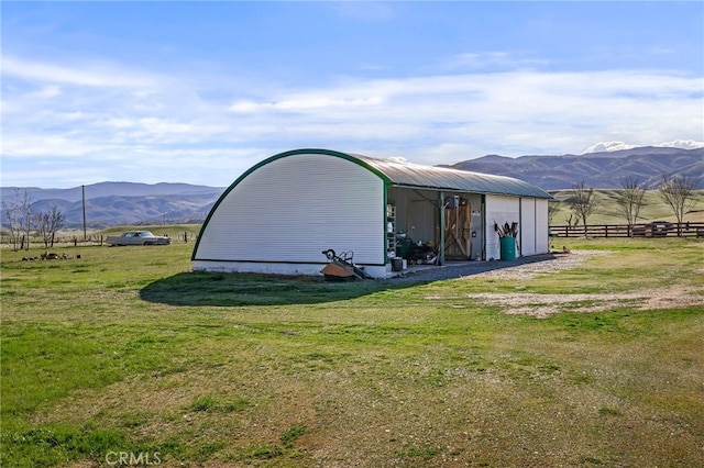 view of pole building featuring a rural view, a yard, fence, and a mountain view