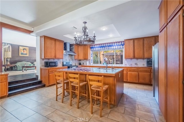 kitchen featuring a breakfast bar, a center island, wall chimney exhaust hood, stainless steel range, and a chandelier