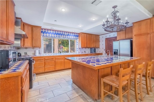 kitchen featuring an inviting chandelier, a kitchen breakfast bar, tile countertops, a kitchen island with sink, and appliances with stainless steel finishes