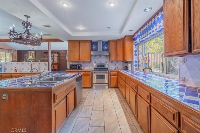 kitchen featuring a notable chandelier, backsplash, a tray ceiling, a center island with sink, and appliances with stainless steel finishes