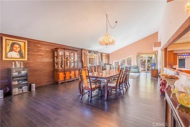 dining space with wooden walls, dark hardwood / wood-style floors, high vaulted ceiling, and an inviting chandelier