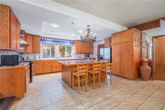 kitchen featuring an inviting chandelier, stainless steel refrigerator with ice dispenser, stove, a breakfast bar area, and a center island with sink