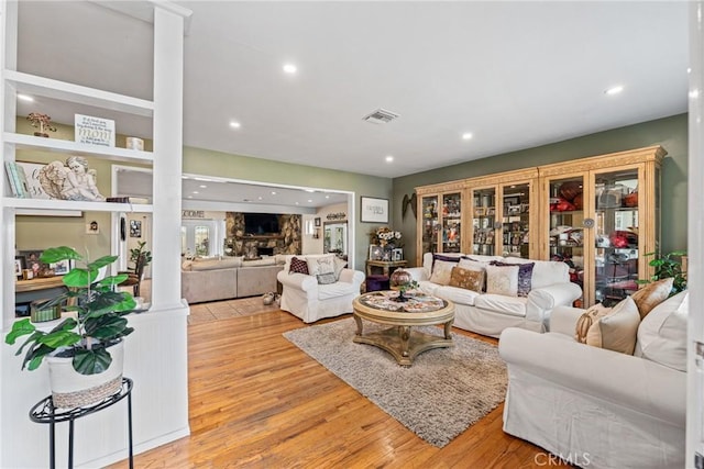 living room with a stone fireplace, decorative columns, and light hardwood / wood-style flooring