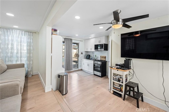 kitchen with white cabinets, tasteful backsplash, appliances with stainless steel finishes, and light hardwood / wood-style flooring