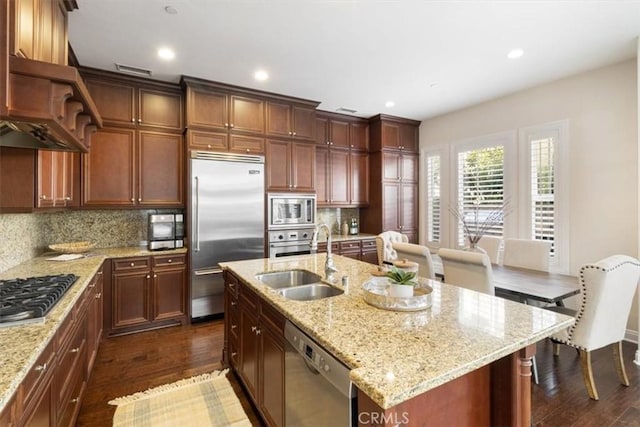 kitchen featuring built in appliances, dark hardwood / wood-style floors, a center island with sink, and tasteful backsplash