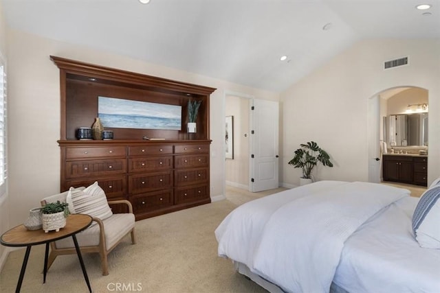 bedroom with light carpet, ensuite bathroom, and vaulted ceiling